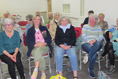 Aelodau o Merched y Wawr Bethel yn eistedd wrth Iola Ynyr mewn rhes ac yn gwenu